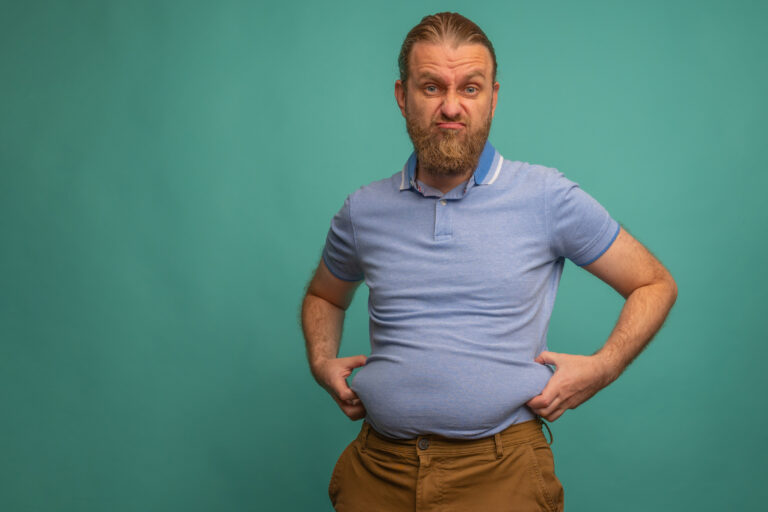 A man with a sad face feels his fat belly on blue background, closeup. Space for text